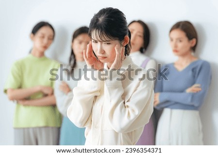 An Asian woman suffers from being excluded from a group of women. Royalty-Free Stock Photo #2396354371