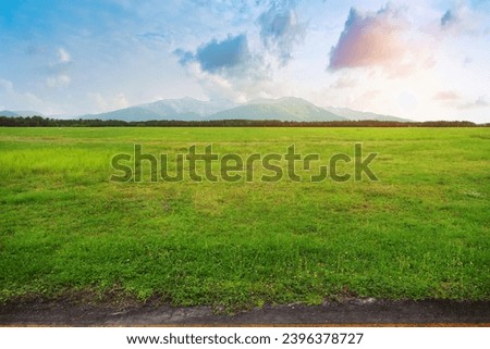 Wide grass landscape beside the road and forest with mountain nature landscape under dramatic sky. Side View on Country Road with beautiful view forrest hills and mountain. Morning sunrise meadow view Royalty-Free Stock Photo #2396378727