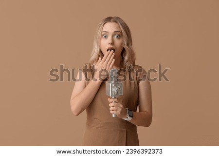 Portrait of shocked female journalist with microphone taking interview on beige background Royalty-Free Stock Photo #2396392373