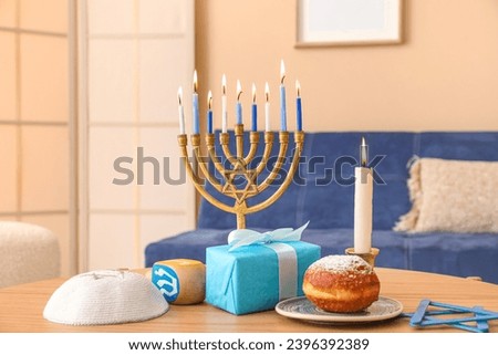Menorah, sufganiyot, kipa and dreidel on coffee table in living room, closeup. Hanukkah celebration Royalty-Free Stock Photo #2396392389