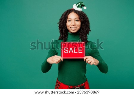 Merry little kid teen girl wear hat casual clothes posing hold in hand card sign with sale title text isolated on plain green background studio. Happy New Year celebration Christmas holiday concept