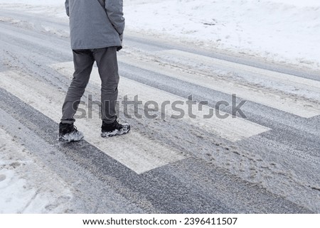 A man crosses a pedestrian crossing that is not properly cleared of snow. He may slip and break his leg. Royalty-Free Stock Photo #2396411507
