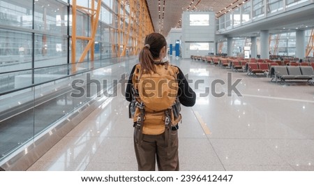 A young Asian woman stands behind in casual clothes and carries a backpack. The schedule can be found on the airport station's scoreboard at weekend. Royalty-Free Stock Photo #2396412447