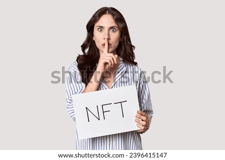 Young Caucasian woman with 'NFT' banner in studio keeping a secret or asking for silence.
