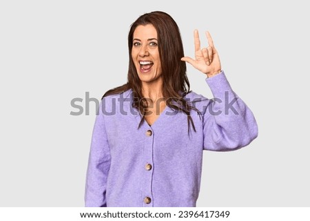 Elegant middle-aged Caucasian woman in studio setting showing a horns gesture as a revolution concept.