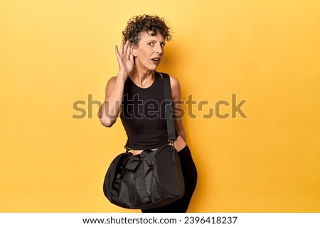 Sportswoman with gym backpack on yellow studio trying to listening a gossip. Royalty-Free Stock Photo #2396418237