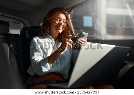 Attractive business woman working on her laptop at the back sit of a car and talking on the phone on the way to meeting.