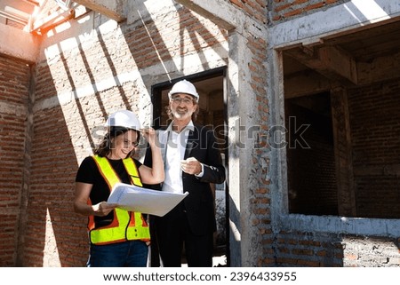 Caucasian female contractor engineer in uniform and hard hat working, inspecting work, happy, work completed according to plan and discussing construction blueprints with senior male business owner  Royalty-Free Stock Photo #2396433955