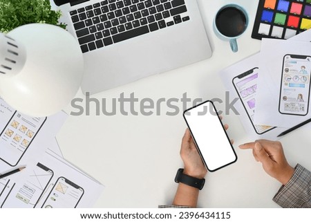 Young creative woman using mobile phone at desk with paper sketches for mobile interface