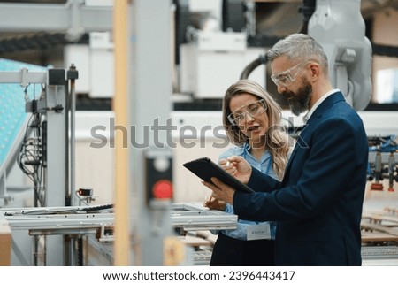 Female engineer and male production manager standing in modern industrial factory, talking about production. Manufacturing facility with robotics and automation. Royalty-Free Stock Photo #2396443417