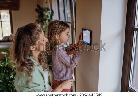 Girl helping mother to adjust, lower heating temperature on thermostat. Concept of sustainable, efficient, and smart technology in home heating and thermostats. Royalty-Free Stock Photo #2396443549