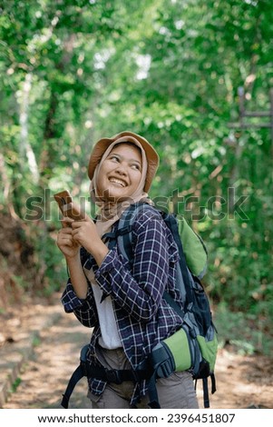 Beautiful Asian hijab backpacker woman wearing a brown hat holding a cell phone while smiling cheerfully
