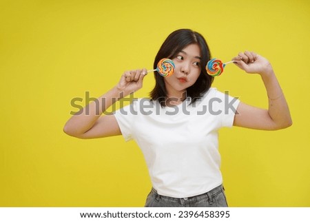 Beautiful Asian young girl holds in hand candy isolated on yellow background