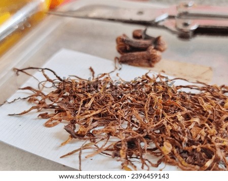 The outside picture focuses on the ingredients for making traditional cigarettes. There is brown tobacco and brown cloves on a white cigarette paper with a blurred background