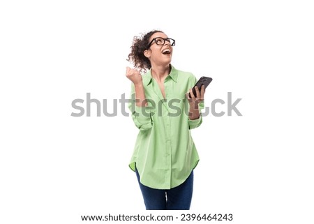 pretty young brunette curly woman in glasses dressed in a green shirt is chatting in a smartphone