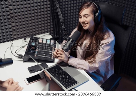 Smiling female podcaster in a striped shirt speaking into a microphone, fully equipped with podcasting gear studio