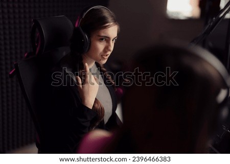 A young woman with braided hair, wearing headphones, in a podcast studio. Her focused expression and the studio's ambient lighting set the stage for a professional recording session