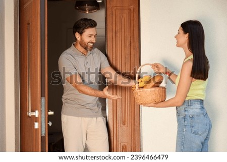 Friendly relationship with neighbours. Young woman with wicker basket of products treating man outdoors Royalty-Free Stock Photo #2396466479