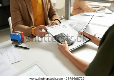 Woman giving her document to get visa Royalty-Free Stock Photo #2396468733