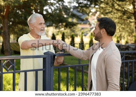 Friendly relationship with neighbours. Happy men shaking hands above fence outdoors Royalty-Free Stock Photo #2396477383