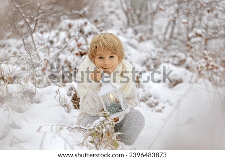 Cute little blond boy, playing in the snow on a winter day, dressed in knitted cloths