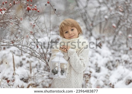 Cute little blond boy, playing in the snow on a winter day, dressed in knitted cloths