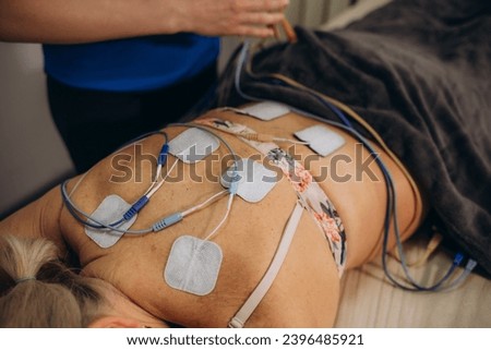 Lower Back Physical Therapy with TENS Electrode Pads, Transcutaneous Electrical Nerve Stimulation. Electrodes onto Patient's Lower Back. High quality photo Royalty-Free Stock Photo #2396485921