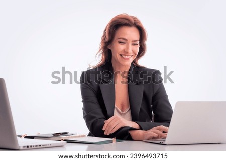 Mid age businesswoman sitting at desk against isolated background. Confident professional female using laptops for work. Copy space.