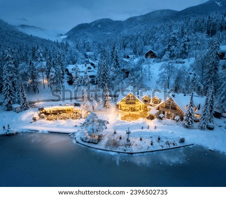 Aerial view of illuminated houses in fairy village in snow, forest, Jasna lake, street lights at winter night. Top view of alpine mountains in fog, snowy pine trees at dusk. Kranjska Gora, Slovenia Royalty-Free Stock Photo #2396502735