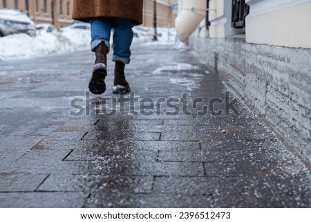 Selective focus on technical salt grains on icy sidewalk surface in wintertime, used for melting ice and snow. Applying salt to keep roads clear and people safe in winter weather from ice or snow Royalty-Free Stock Photo #2396512473