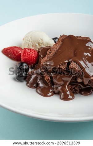 Chocolate flowing on brownie with ice cream and fresh berry. Delicious chocolate cakes with chocolate glaze on a blue background table.