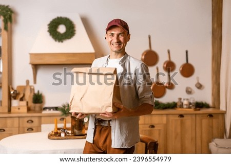 a delivery man with a package of food stands in a Christmas interior