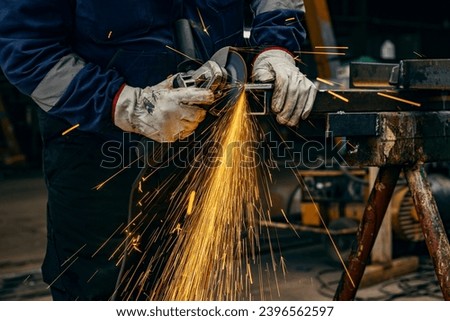 Close up of heavy industry worker's hands grinding in metallurgy factory. Royalty-Free Stock Photo #2396562597