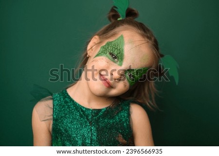 A cheerful girl with painted eyes with the image of dragon wings - the symbol of the new year 2024 on a green studio background