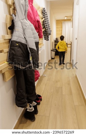 Snow clothes hanging on a hanger on the wall and boots on the floor in the entrance hall of the holiday apartment, Spain Royalty-Free Stock Photo #2396572269