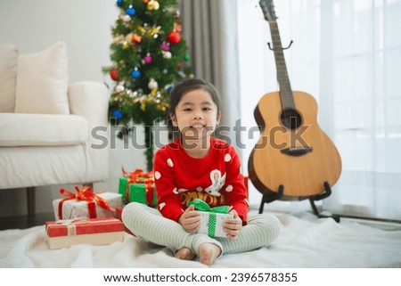 Christmas, x-mas, winter concept. Asian baby child girl holding gift boxes smiling happy cheerful. Celebrates the Happy New Year near the Christmas tree in a living room at home.