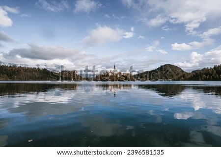 Lake Bled in Slovenia. Charming autumn panorama landscape of island with church rounded colorful trees in the middle of Bled lake. Colorful autumn scenery, popular travel destination.
