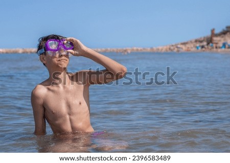 Handsome teen grins with a diving mask, embracing the beach's playful atmosphere on a warm and sunny day. Royalty-Free Stock Photo #2396583489