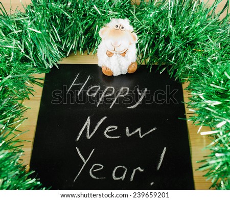  		 on the black Board, white chalk written "happy new year" on the background of green tinsel and white sheep