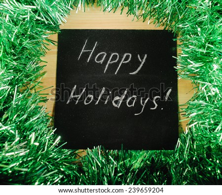  		 on the black Board, white chalk written "happy nholidays" on the background of green tinsel.