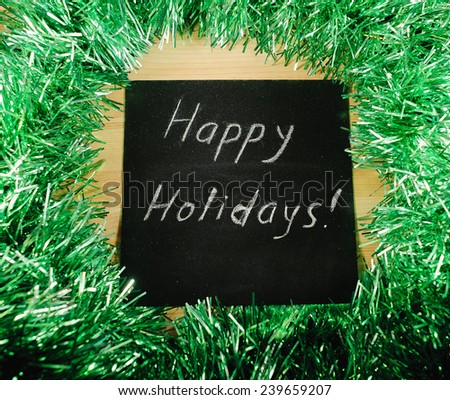  		 on the black Board, white chalk written "happy nholidays" on the background of green tinsel.