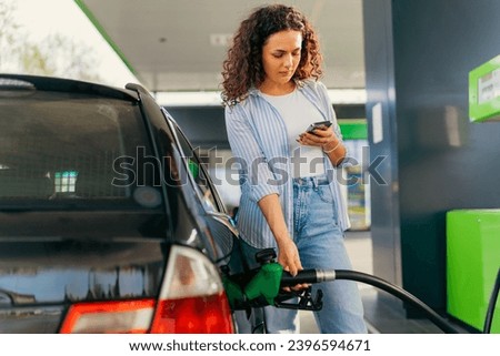 A young beautiful woman does not follow the safety rules and uses the phone while filling her car gas tank