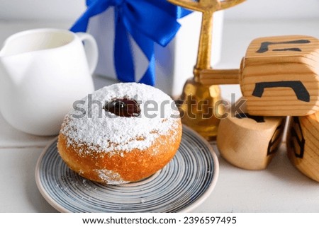 Tasty donut, milk and dreidels for Hanukkah celebration on light wooden table, closeup
