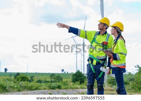 Maintenance engineer team worker building looking for wind turbines blueprint drawings and point finger on windmill field farm Alternative renewable energy for clean energy concept.