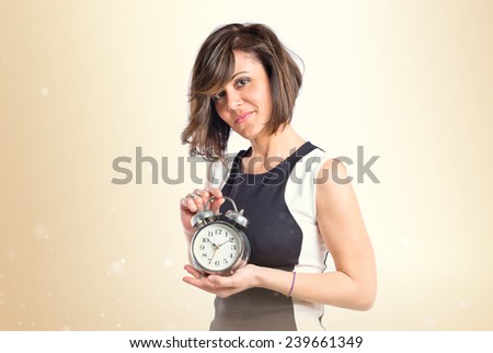 Pretty woman holding an antique clock over ocher background 