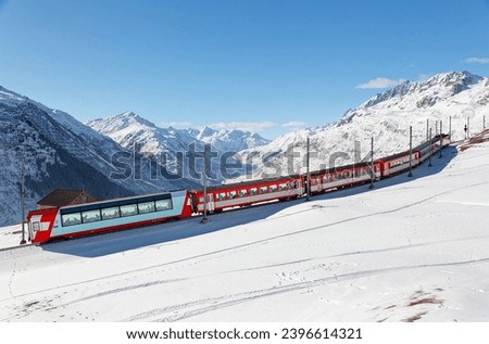 Tourists ride on a Glacier Express of Matterhorn Gotthard Railway on a sunny winter day, enjoying the view thru panoramic windows of snowy mountains under blue clear sky in Andermatt, Uri, Switzerland Royalty-Free Stock Photo #2396614321