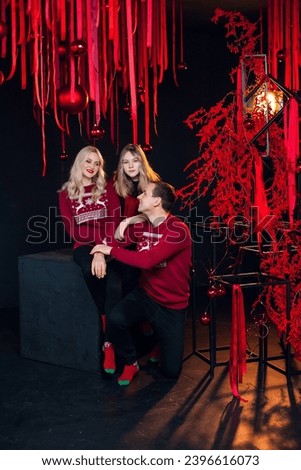 Beautiful cheerful family dressed in New Year's red clothes in an atmospheric photo studio with a stylish festive interior in red colors.