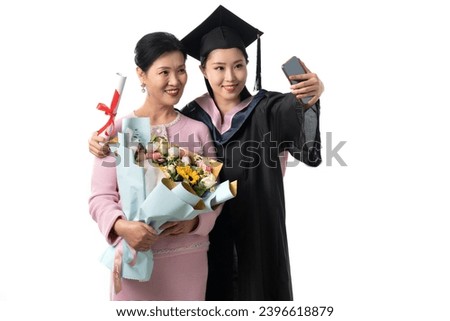 Daughter and mother wearing graduation dresses taking photos with mobile phones