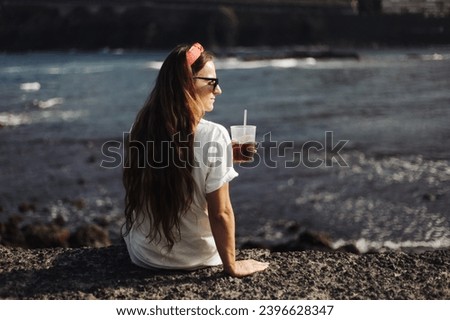 Woman drinking Sangria by the sea shore. Sunny day cold cocktail. Long hair girl. Holiday alcohol drinking. Sunset colors. Sunglasses person. Lifestyle background.