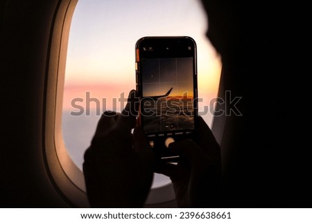 Travel by plane. A woman hands holding a smartphone and taking pictures during an amazing sunset, view from the airplane window. Sunset above the clouds.